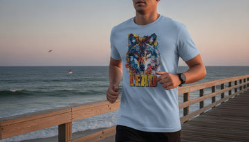 Person jogging at dawn on a boardwalk wearing a light blue wolf tee with the design fully visible against a pink-blue sky and ocean.