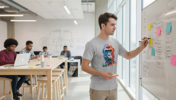 Person in a Sport Grey gorilla graphic tee stands at a whiteboard in a sunlit coworking space mid-brainstorm.
