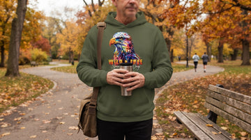 A person in a military green eagle-print hoodie walks a park path in autumn, holding a travel mug.