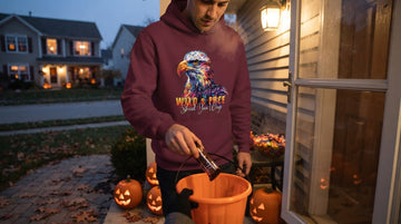 A person wearing a maroon eagle graphic hoodie hands candy to a trick-or-treater on a porch decorated with glowing carved pumpkins at dusk.