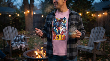 A man wears a pink wolf graphic tee under an open charcoal flannel at a backyard fire pit on a cool evening.