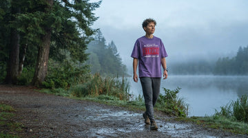 A person in a printed quote T-shirt walks beside a misty lake on an overcast early morning.
