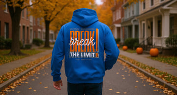A person in a royal blue hoodie walks down a quiet tree-lined street in late October, with leaves on the ground and porch pumpkins behind.