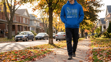 Person wearing a royal blue hoodie walking along a neighborhood street on an autumn morning with hands in the kangaroo pocket.