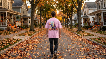 Person wearing a blossom pink t-shirt walking down a leaf-covered street at golden hour with pumpkins on nearby porches.