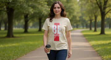 A person in a Be Yourself tee walks a tree-lined path in soft morning light, holding a travel mug.