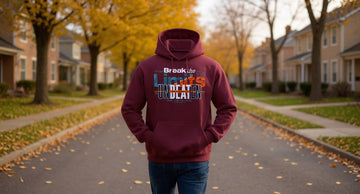 A man in a maroon hoodie walks down a tree-lined suburban street in autumn, hands in the front pocket, leaves on the ground.